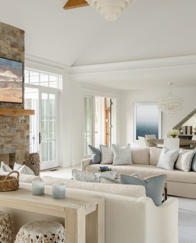 Cream sofas and white walls in a bright, coastal living room with stone fireplace.