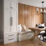 Built-in white dining bench with grey cushions against a vertical wood paneled wall.