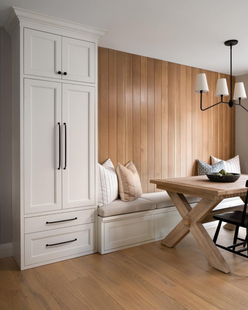 Built-in white dining bench with grey cushions against a vertical wood paneled wall.