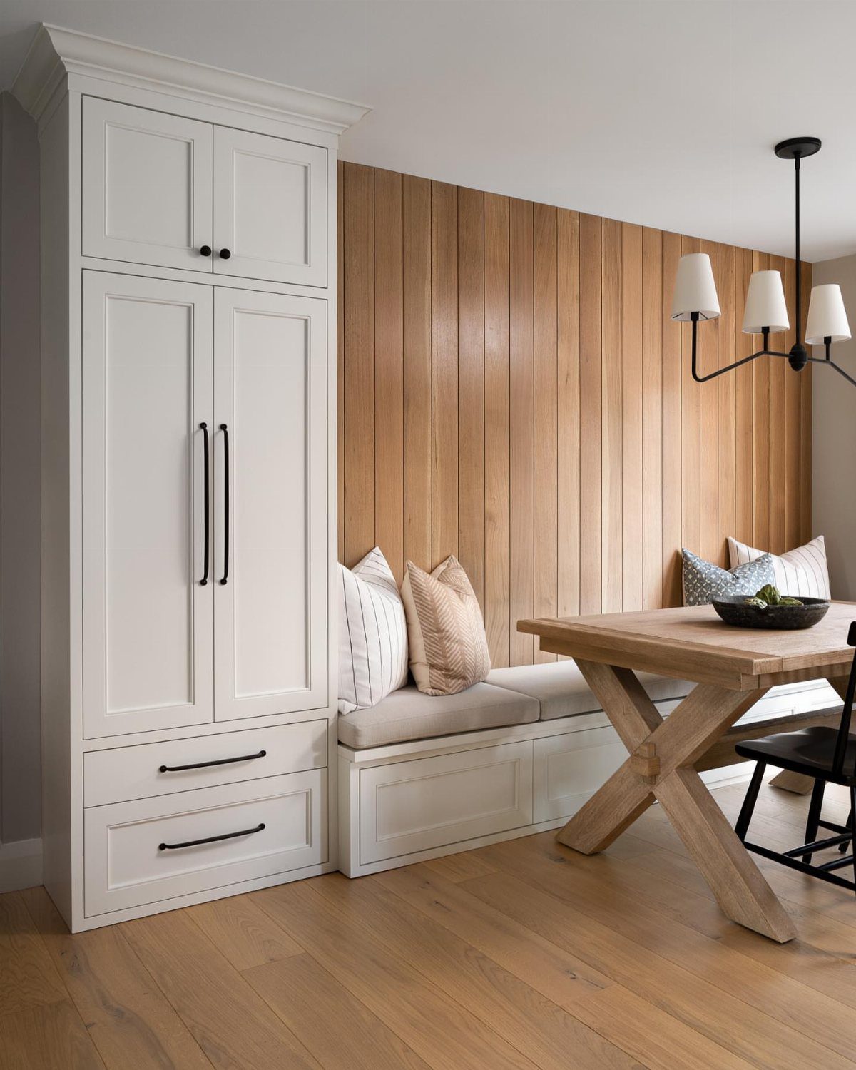 Built-in white dining bench with grey cushions against a vertical wood paneled wall.
