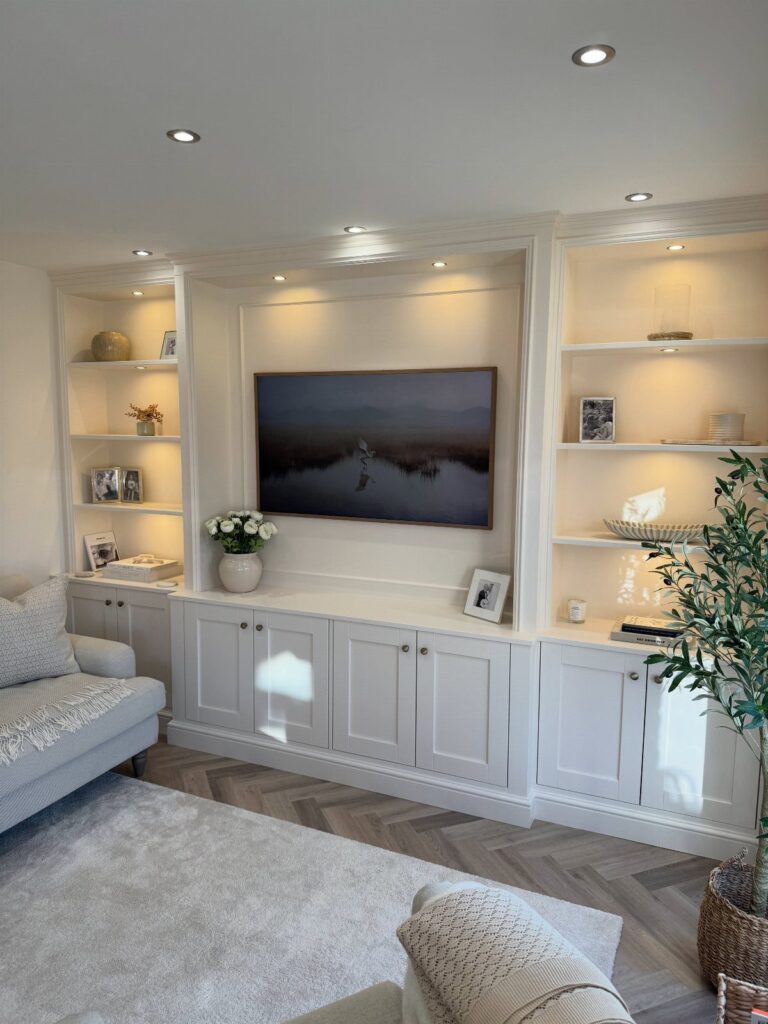 White built-in entertainment center with integrated lighting, shelving, and a wall-mounted television.