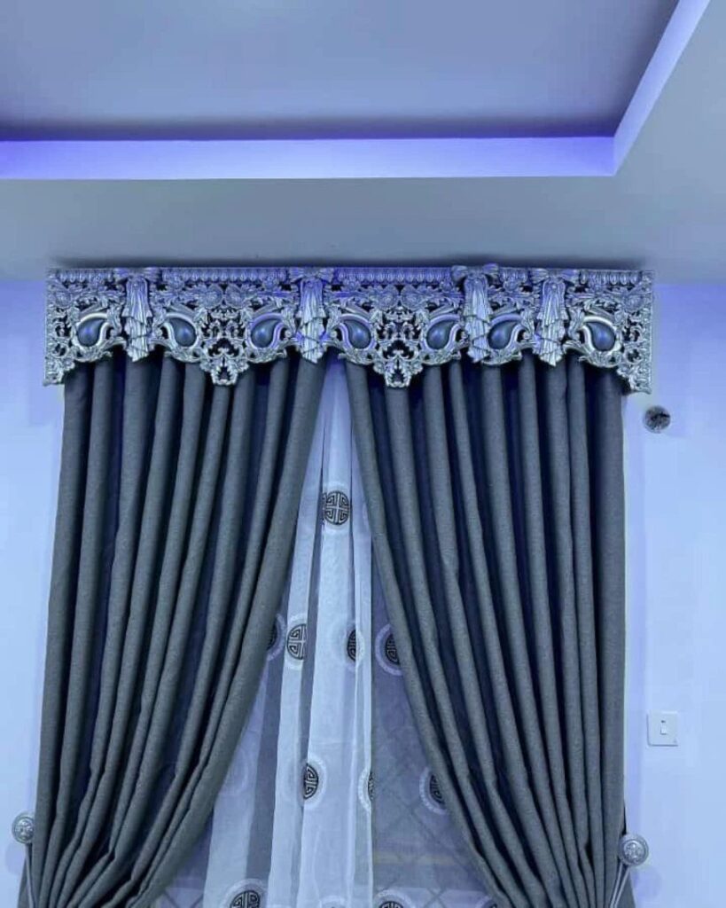 Grey pleated curtains and white sheers topped with an ornate silver decorative valance.