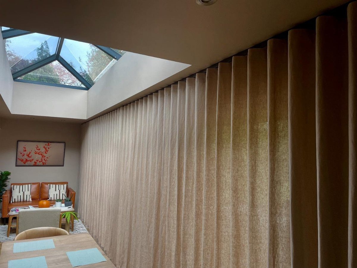 Beige linen curtains covering a large wall in a modern room with skylight
