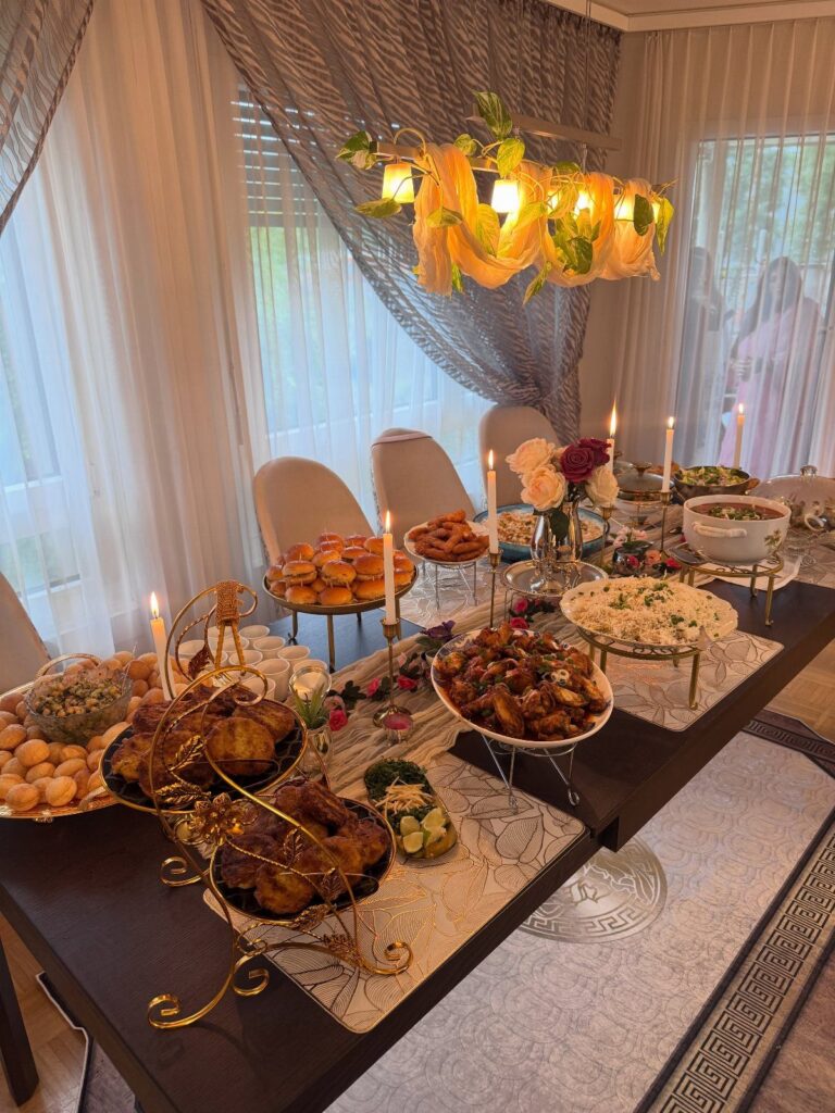 Dinner table decorated with food platters, white candles, and flowers under a yellow chandelier.