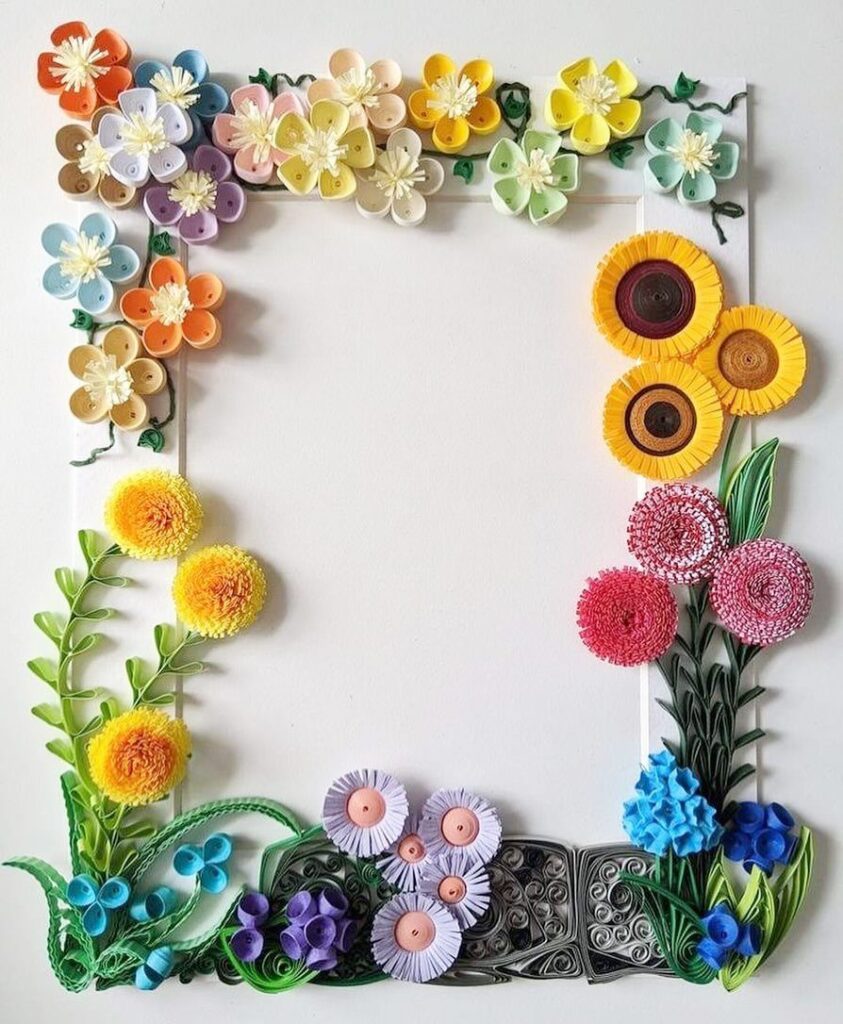 White picture frame decorated with colorful quilled paper flowers and green leaves.