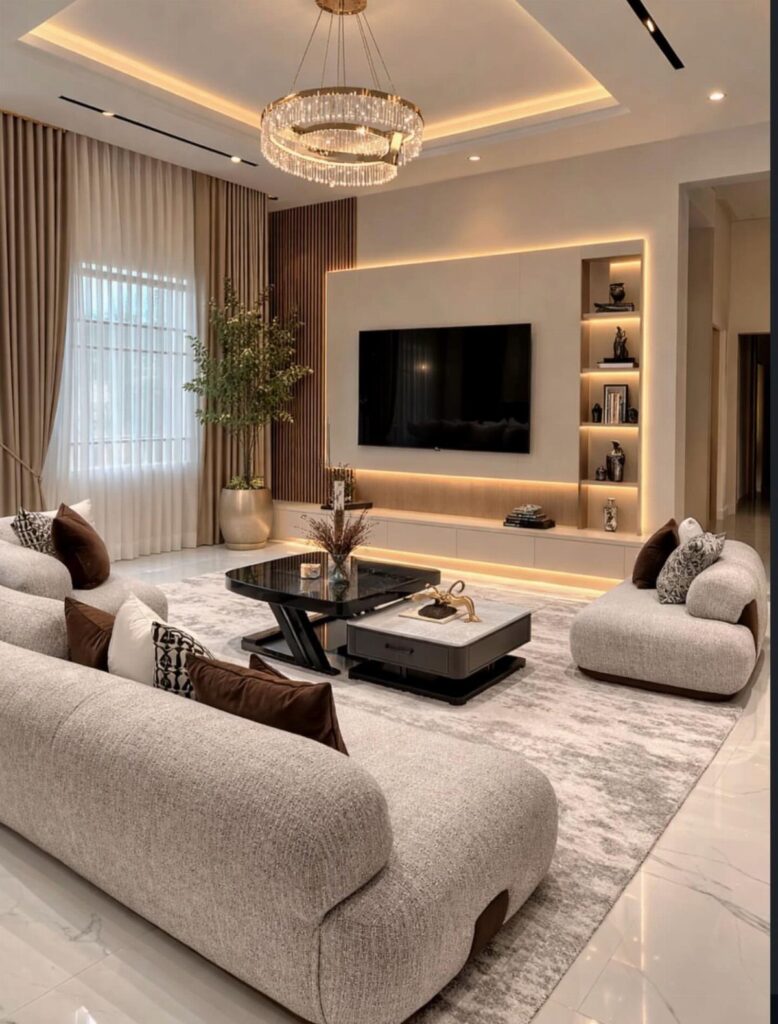 Modern drawing room with beige sofas, crystal chandelier, and backlit TV wall panel.