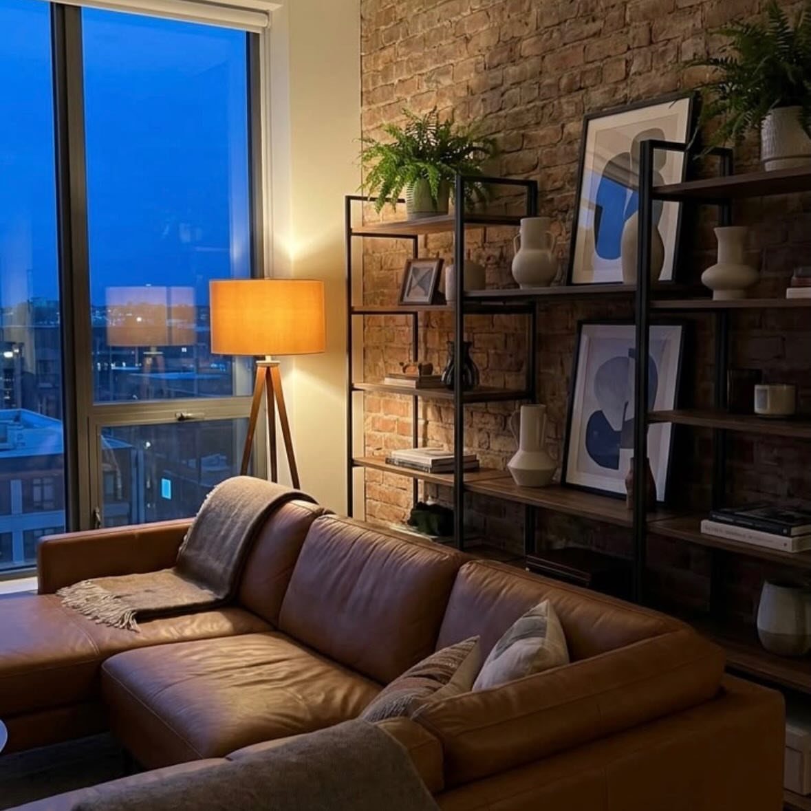 Brown leather sofa and black shelving against a red exposed brick wall.