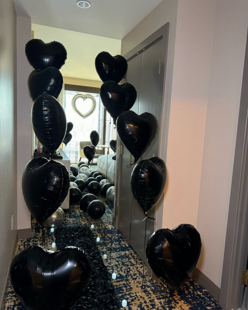 Black heart-shaped balloons filling a hotel room hallway for a romantic decoration setup.