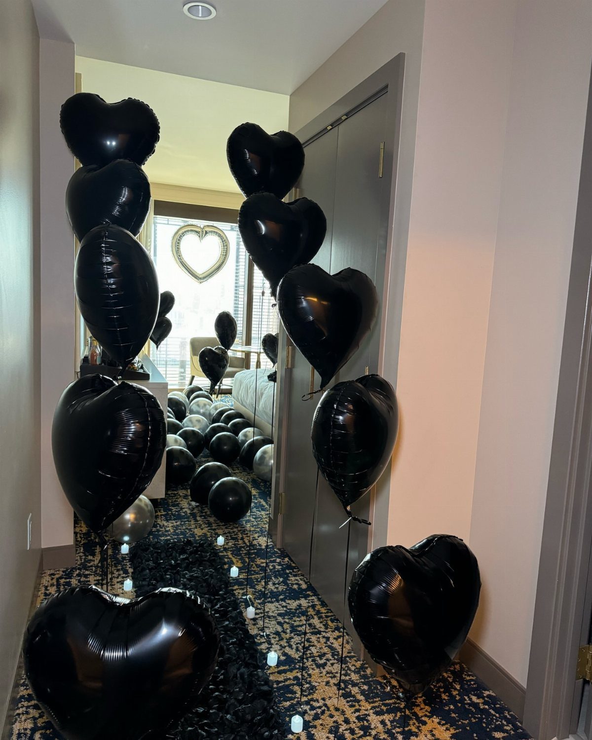 Black heart-shaped balloons filling a hotel room hallway for a romantic decoration setup.