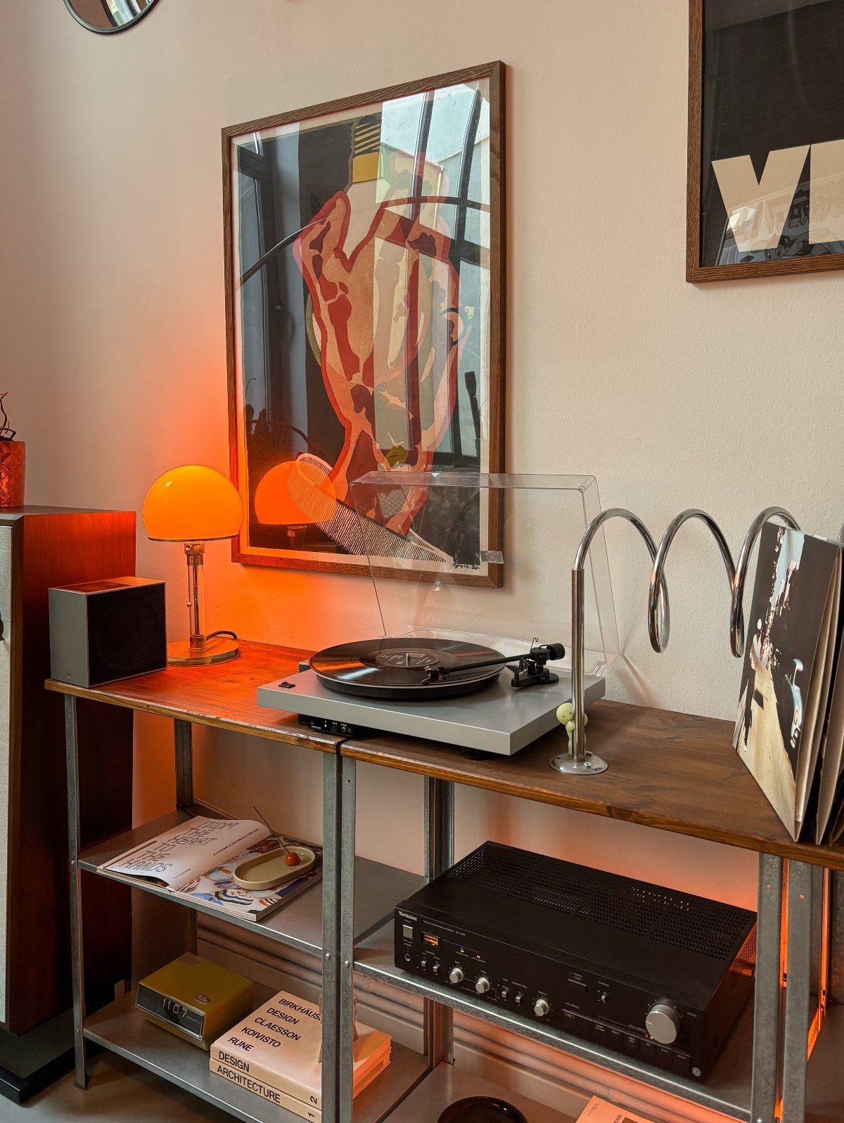 Wooden console table with record player, orange lamp, and abstract wall art.