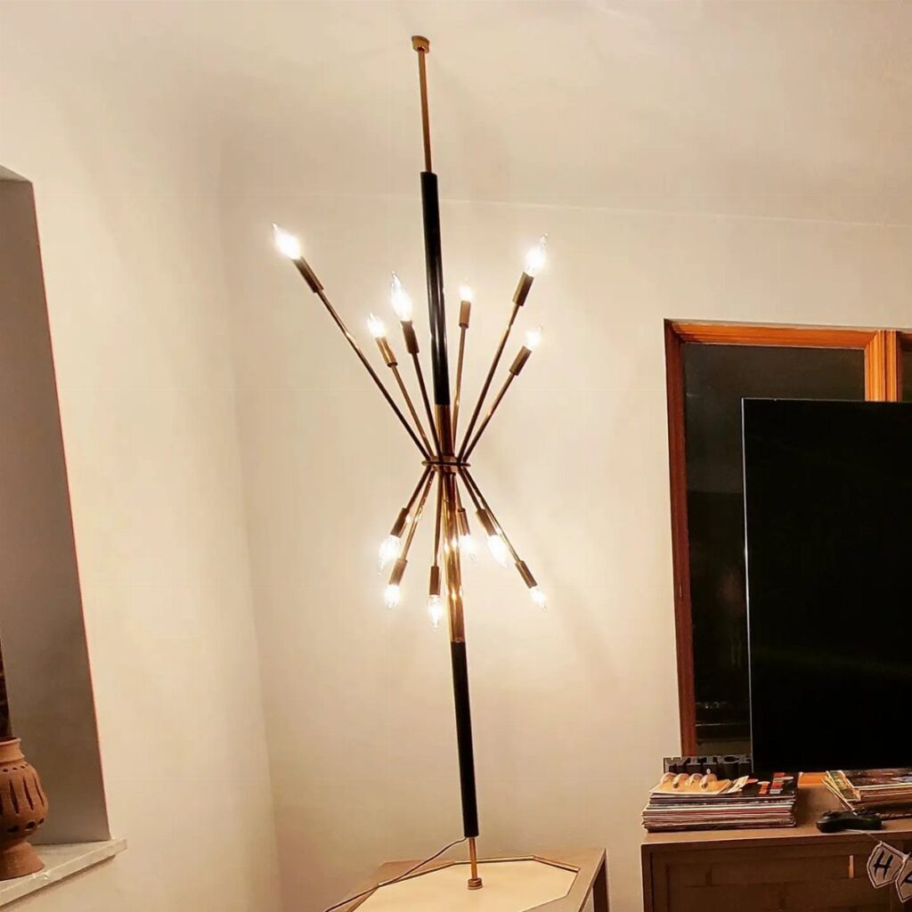 Sputnik chandelier lamp with radiating gold arms and bulbs against a white wall.