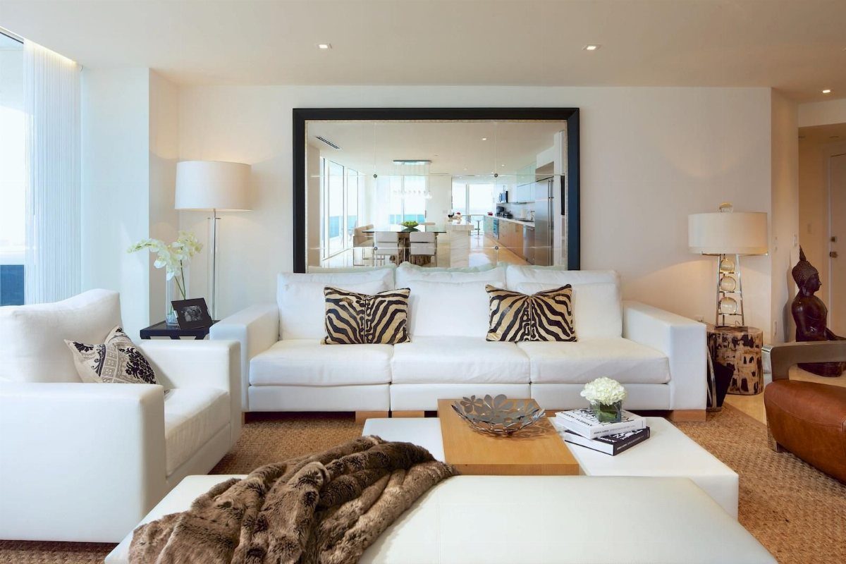 Large rectangular mirror with black frame hanging above a white modern sofa.