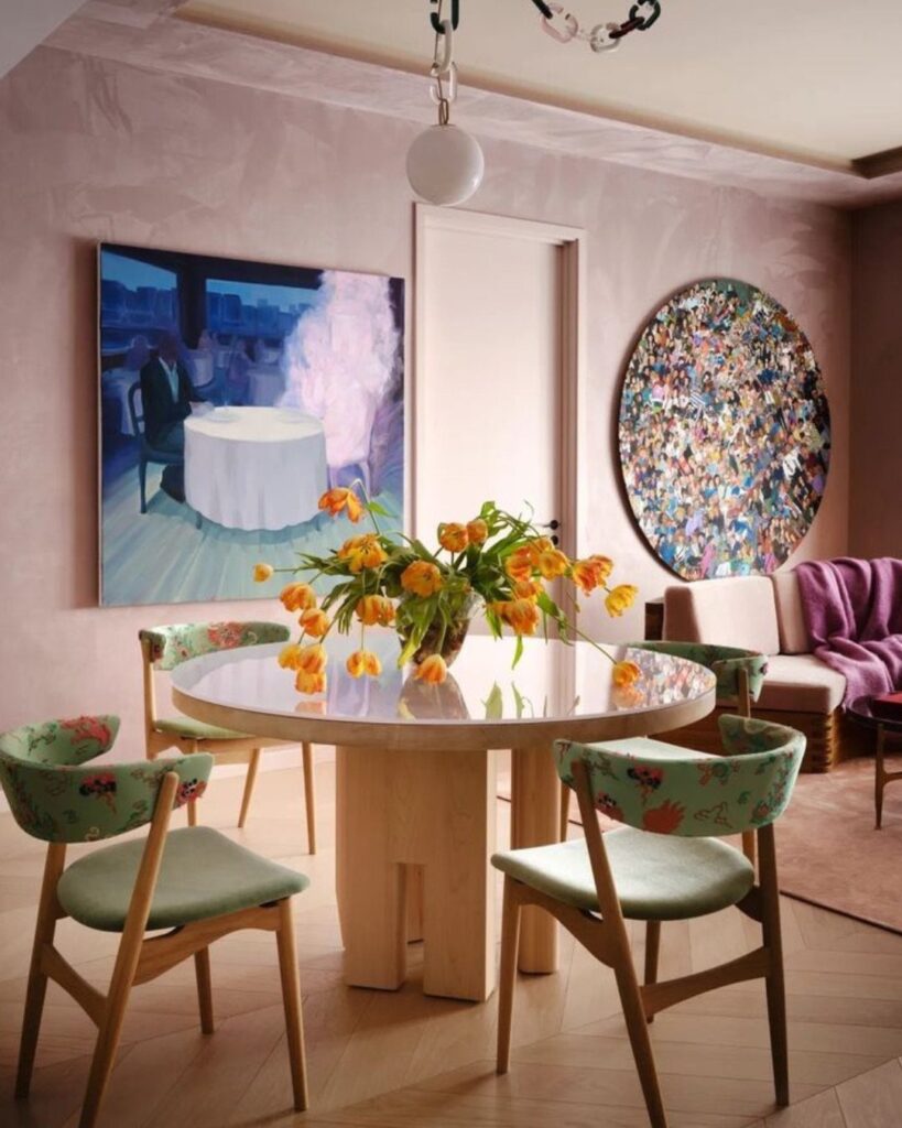 Dining room with pink walls, green floral chairs, and a round white table.