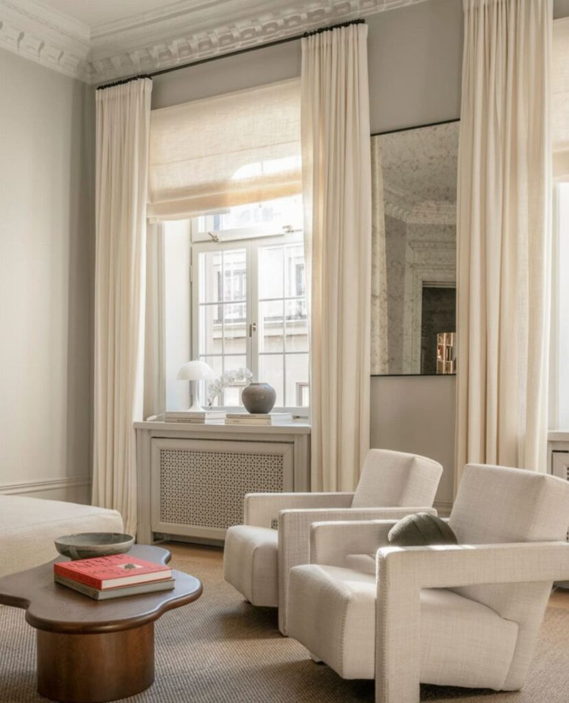 Cream curtains and a roman shade framing a window in a modern living room.