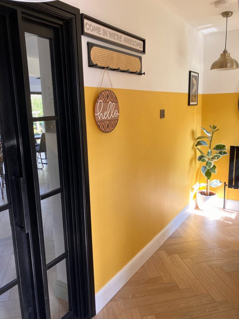 Yellow and white horizontal half-painted walls in a hallway with herringbone wood floors.
