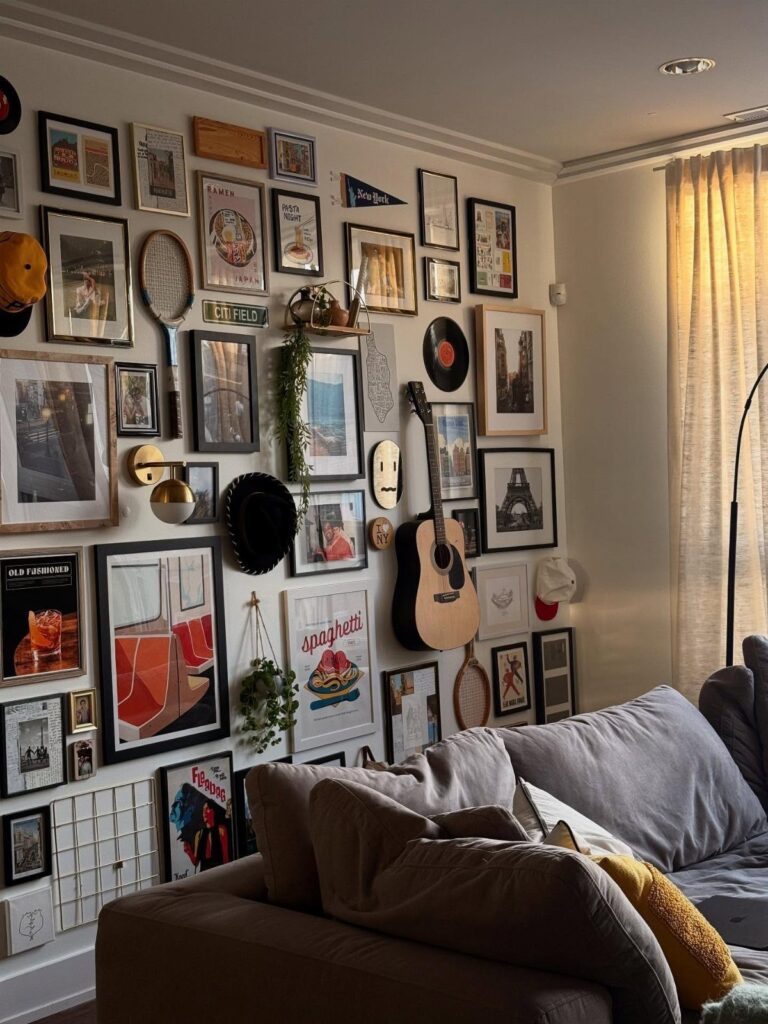 Gallery wall with eclectic framed art and a guitar above a grey couch.